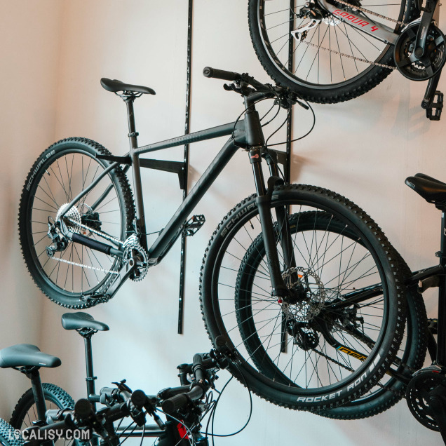 Une collection de vélos de différents styles et tailles, avec une prédominance de VTT aux pneus épais et aux cadres robustes montés sur un présentoir mural dans le magasin de vélo Total Bike à Liège.