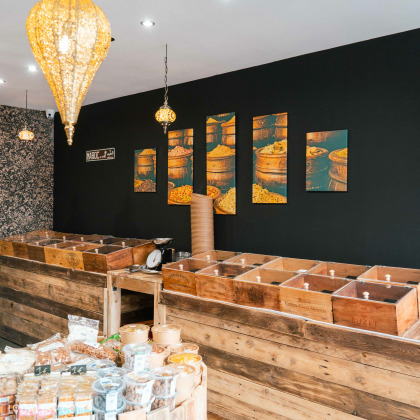 Comptoir en bois de la boutique  Le Panier du Sud avec des bacs d'épices en vrac, décoré de photos de pots d'épices. Ambiance chaleureuse avec des luminaires orientaux suspendus.