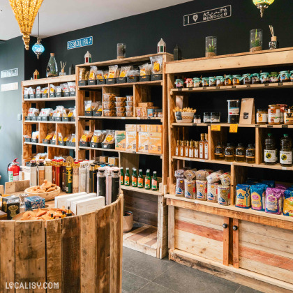 Étagères en bois remplies de produits d'épicerie fine du magasin Le Panier du Sud à Verviers, comme des épices, huiles, sauces et confitures, dans une boutique à l'ambiance chaleureuse avec des décorations marocaines.