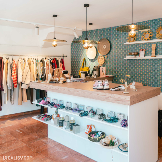 Intérieur de la boutique ''Choisyr'' à Spa avec un comptoir central exposant des accessoires, bijoux et chaussures, entouré de vêtements suspendus et d'une décoration murale colorée.