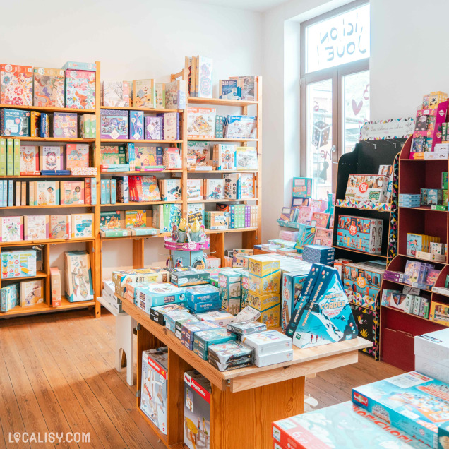 Vue intérieure de la Librairie Long-Courrier à Tilff, mettant en avant des étagères garnies de livres, jeux, puzzles et créations d'enfants.