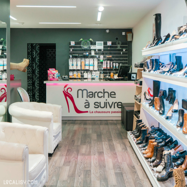 Intérieur de la boutique "Marche à Suivre" à Ans, mettant en avant un comptoir moderne et des étagères remplies de chaussures élégantes, avec un coin salon confortable pour les clients.