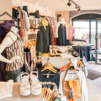 Des mannequins habillés, des vêtements suspendus sur des cintres, des chaussures et des sacs à main exposés au magasin de vêtements Miss Fripe à Hamoir. Le magasin est bien éclairé et organisé, avec une variété de vêtements et d'accessoires pour femmes.