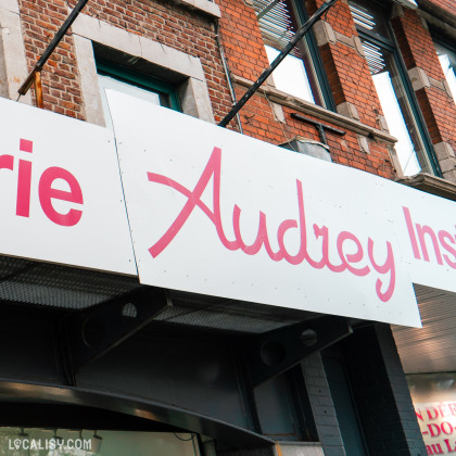 Devanture de la Parfumerie Audrey à Chênée. On y voit une enseigne blanche avec le texte "Audrey" en rose sur un bâtiment en briques rouges.