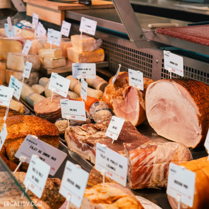 Une variété de produits de charcuterie, tels que du jambon, du saucisson, et d'autres viandes, avec des étiquettes indiquant les noms et les prix des produits dans la boucherie Simonis Boucherie Traiteur à Plainevaux. Les étiquettes incluent des noms comme "Jambon Cuit", "Saucisson", "Filet de Porc", et "Lard Salé".