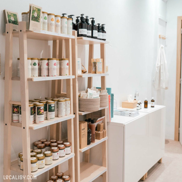 L'intérieur du magasin de cosmétiques Nativis à Verviers, avec deux étagères en bois remplies de divers produits, tels que des bouteilles de savon liquide, des boîtes de conserve, des paniers contenant des articles divers, et des emballages en carton.