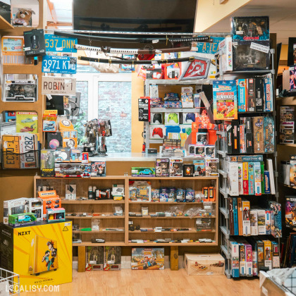 L'intérieur du magasin de jeux vidéo All4Addicts à Verviers, le magasin est rempli de divers articles de collection, jouets, jeux de société, et accessoires électroniques. On peut voir des étagères remplies de boîtes de jeux, des figurines, des voitures miniatures, des puzzles, et des accessoires pour consoles de jeux.