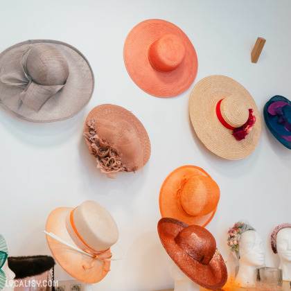 Une collection de chapeaux élégants accrochés au mur la Chapellerie Le Chapeau d'Or à Liège. Les chapeaux sont de différentes couleurs et styles, y compris des chapeaux de paille, des chapeaux ornés de fleurs et des chapeaux avec des rubans.