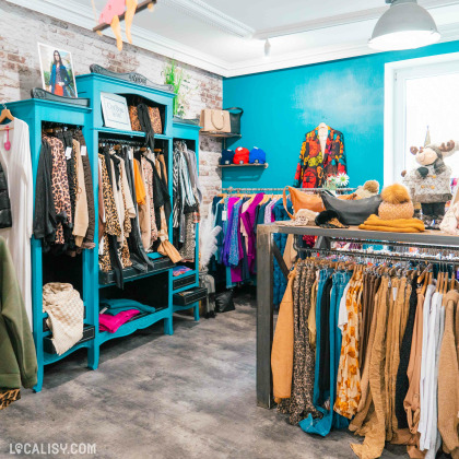 L'intérieur du magasin de vêtements pour femmes Black Lemon Store à Welkenraedt avec des vêtements suspendus sur des cintres et des étagères. Les vêtements incluent des motifs léopard, des couleurs vives et des textures variées. Il y a également des accessoires comme des sacs à main et des chapeaux exposés.