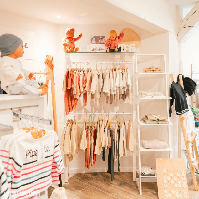 L'intérieur du magasin de vêtements pour enfants et bébés King & Queen Kids à Spa, avec des vêtements suspendus sur des cintres, organisés par taille et type, avec des étagères contenant des vêtements pliés. Il y a également des mannequins habillés pour exposer les vêtements.