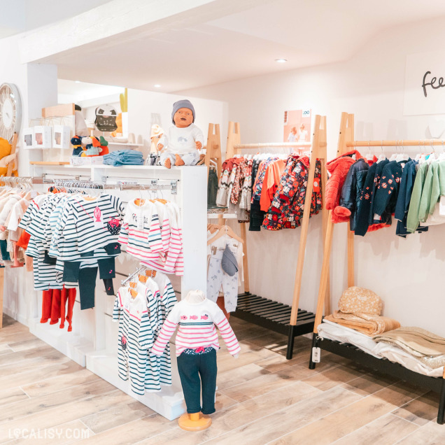 L'intérieur du magasin de vêtements pour enfants et bébés King & Queen Kids à Spa, avec des vêtements colorés et variés pour enfants, accrochés sur des cintres et des étagères. Il y a des mannequins habillés avec des tenues pour enfants, et des vêtements pliés sur des étagères.