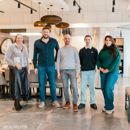 Cinq personnes debout dans le magasin de luminaires Espace Design à Sprimont. Le magasin présente un intérieur moderne avec des luminaires suspendus au plafond, des meubles élégants et une décoration soignée. Les personnes sont habillées de manière décontractée et se tiennent devant une table et des chaises.