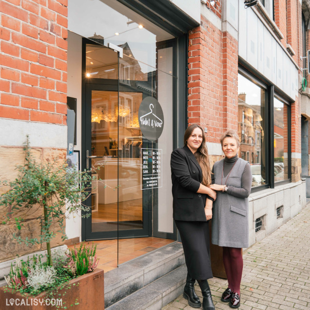 Devanture du magasin de vêtements Habit&Vous à Tiff. Deux personnes se tiennent devant la porte en verre du magasin, qui est encadrée par des murs en briques rouges. Sur la porte, il y a un panneau indiquant les horaires d'ouverture.