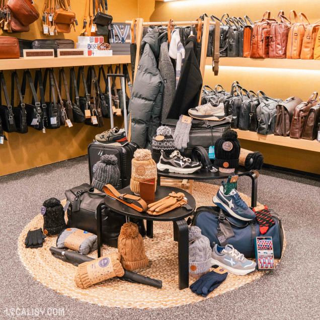 L'intérieur du magasin de maroquinerie Maroquinerie Klein à Verviers, avec une présentation soignée de divers articles de mode et accessoires. On y voit des sacs à main, des sacs à bandoulière, des manteaux, des chaussures, des gants, des bonnets, des écharpes et des chaussettes. Les articles sont disposés sur des étagères et des tables, avec une attention particulière à l'organisation et à l'esthétique.