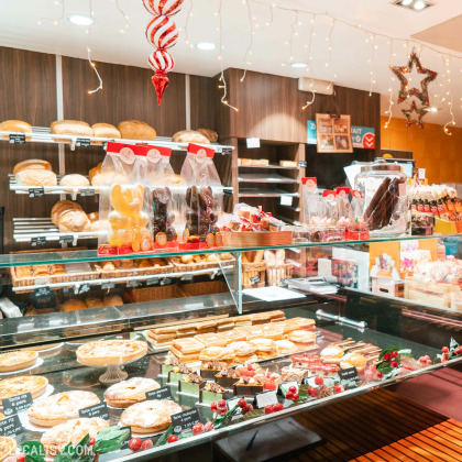 L'intérieur de la Boucherie Charcuterie Vanderbyse à Villers-L'Evêque bien éclairée et décorée, avec des étagères remplies de pains variés à l'arrière-plan. Sur le comptoir en verre, il y a une variété de pâtisseries, tartes, et gâteaux exposés, ainsi que des chocolats emballés et d'autres confiseries.