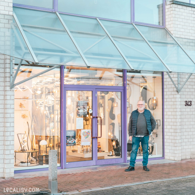 Devanture du magasin de luminaires Mabrilux à Welkenraedt. La façade est en verre avec une structure métallique et des portes violettes. À travers les vitrines, on peut voir divers luminaires exposés à l'intérieur. Un homme se tient devant le magasin.