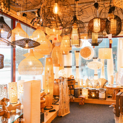 L'intérieur du magasin de luminaires Mabrilux à Welkenraedt, avec une grande variété de lampes suspendues et de lampes de table, principalement en matériaux naturels comme le rotin et le bambou. Les luminaires sont de différentes formes et tailles, créant une ambiance chaleureuse et accueillante grâce à l'éclairage doux et diffus.