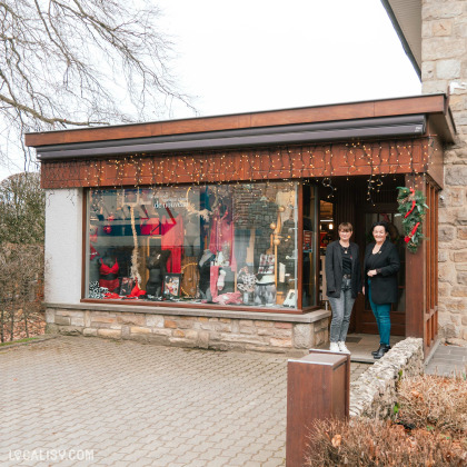 Devanture du magasin de lingerie Lingerie Huppertz à Waimes. La vitrine est décorée avec des guirlandes lumineuses et expose divers articles de lingerie, principalement en rouge et noir. Deux personnes se tiennent à l'entrée du magasin, qui est décorée avec une couronne de Noël.