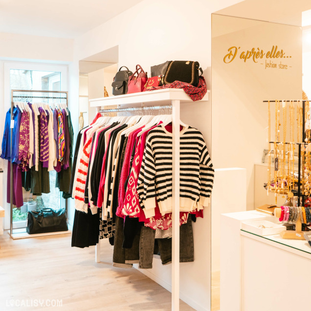 Intérieur de la boutique D'après Elles Fashion Store à Comblain-au-Pont avec une tringle de pulls.