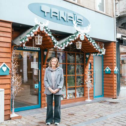 Devanture du magasin Tanaïs à Verviers - Façade en bois avec une décoration festive composée de guirlandes, lanternes et rennes. Une personne souriante se tient devant l'entrée accueillante du magasin.