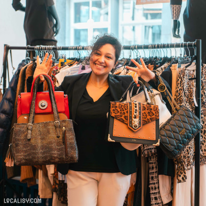 Commerçante souriante présentant des sacs à main dans le magasin de seconde main à Spa.