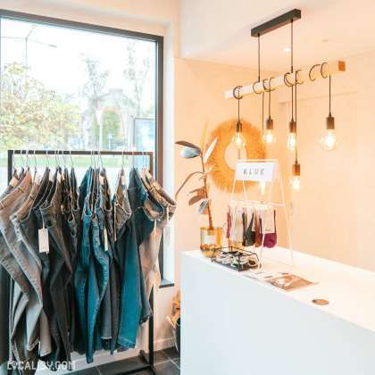 Espace caisse et présentation de jeans – Comptoir blanc moderne avec éclairage design et présentoir de jeans et accessoires stylés, créant une ambiance minimaliste et chaleureuse.