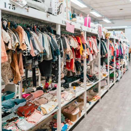 Rayons de vêtements pour enfants – Longs étalages remplis de vêtements d’occasion pour enfants, bien organisés sur cintres et étagères. Divers accessoires et chaussures sont également exposés.