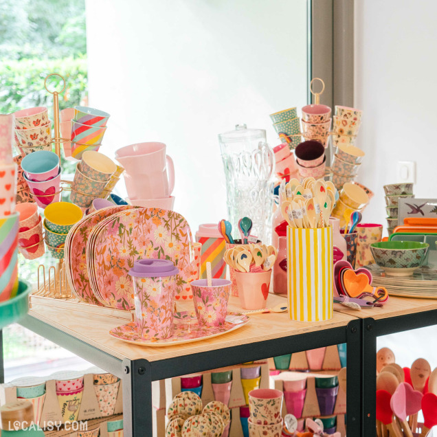 Espace dédié aux démonstrations et ateliers à L’Appart Concept Store, avec une grande table conviviale entourée de chaises et des présentoirs d’articles de cuisine.