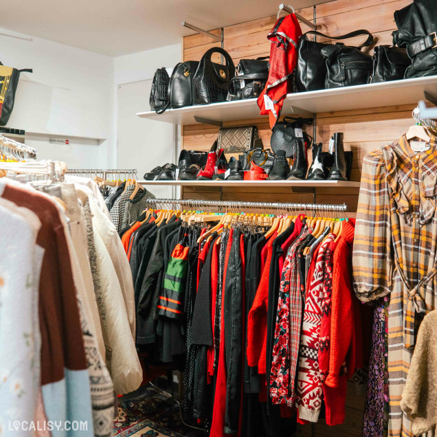 Sélection de vêtements colorés et sacs exposés chez Canopée, magasin de seconde main pour femmes à Malmedy.