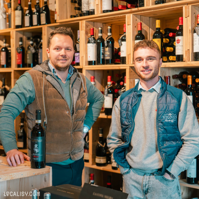 Magasin de vins et spiritueux Les Vignes en Ville à Beaufays – portrait des gérants devant des étagères remplies de bouteilles de vin.