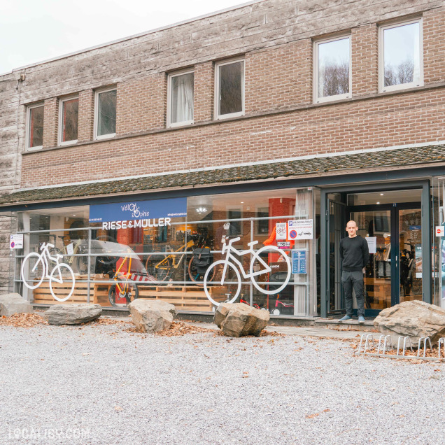 Façade du magasin Vélo d'Opale avec le logo de la marque Riese & Müller, des vélos exposés en vitrine et une personne debout devant l'entrée.