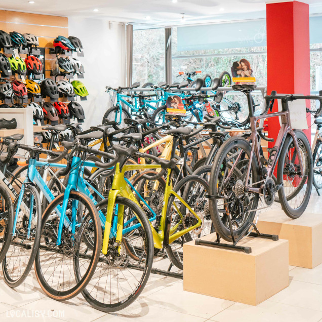 Salle d'exposition de vélos de route et accessoires dans le magasin, avec des casques colorés accrochés au mur et une variété de vélos exposés.