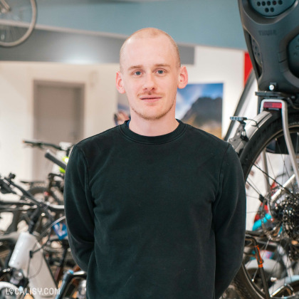 Portrait d'un employé du magasin souriant, avec des vélos et accessoires en arrière-plan dans un espace lumineux.