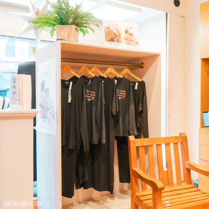 Un présentoir intérieur de la boutique, mettant en avant des vêtements noirs élégants sur des cintres, avec une décoration chaleureuse et des plantes.