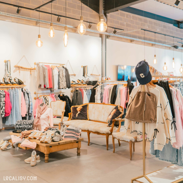 Intérieur du magasin Clothing Rose à Aywaille montrant des rangées de vêtements élégants suspendus dans un cadre moderne et lumineux.