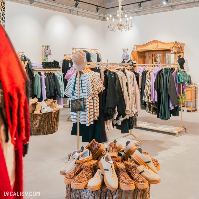 Présentation de chaussures tendance et vêtements dans le magasin Clothing Rose à Aywaille, disposés sur des troncs en bois décoratifs.