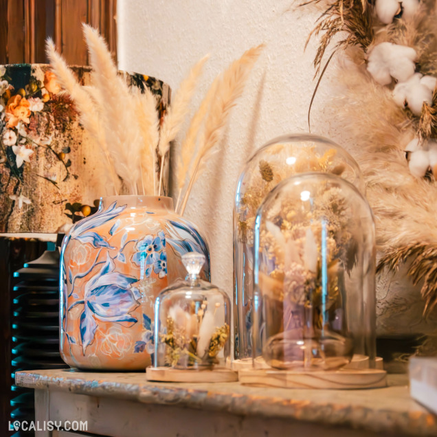 Objets décoratifs et fleurs sous cloches en verre au magasin L'Atelier des Fleurs à Stavelot.