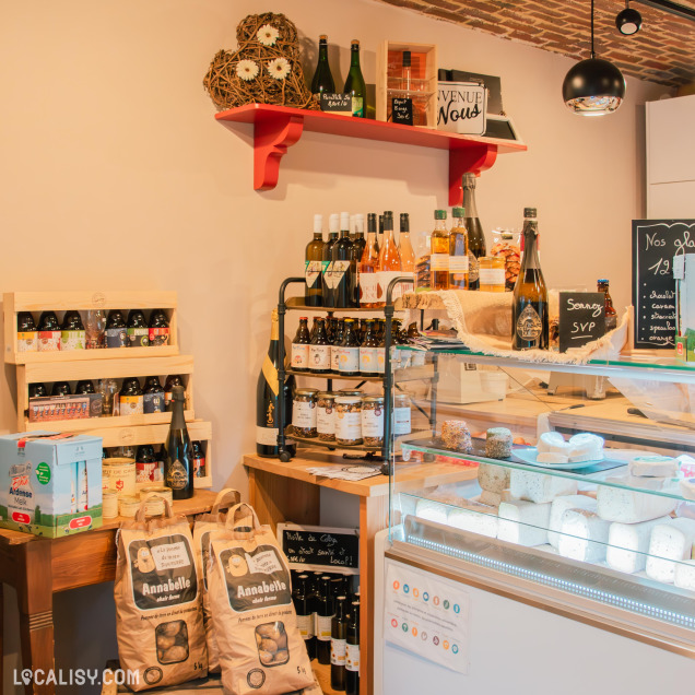 Une vue détaillée de l’espace épicerie du magasin, mettant en avant une sélection de produits locaux, tels que des bières artisanales, du vin, des confitures et des sacs de pommes de terre Annabelle, posés sur des étagères en bois.