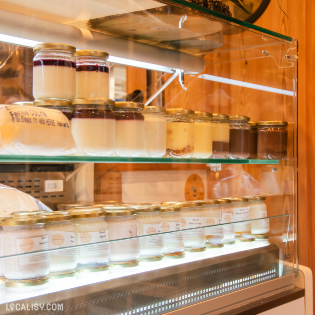 Une vitrine réfrigérée contenant une variété de desserts lactés en pots en verre, avec des saveurs allant du chocolat à la vanille, en passant par des yaourts aux fruits et des crèmes dessert. L'éclairage met en valeur la qualité artisanale des produits.