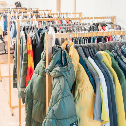 Sélection de vestes et manteaux suspendus dans la boutique Les Fééries by Val-Lou, avec des modèles variés allant du doudoune épaisse aux vestes plus légères, organisés par couleur et taille.