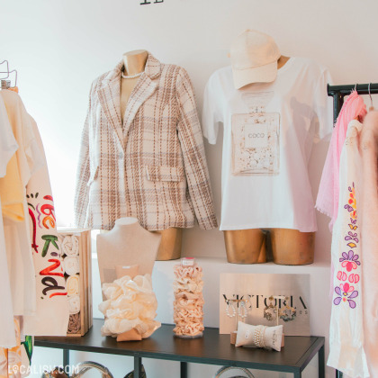 Détails sur des mannequins : Deux mannequins sont habillés avec un style chic et décontracté : l'un porte une veste à carreaux beige et blanc, tandis que l'autre arbore un t-shirt blanc imprimé "COCO" et une casquette assortie. Sur une table en métal noir, plusieurs accessoires comme des bijoux et des chouchous en tissu sont soigneusement exposés.