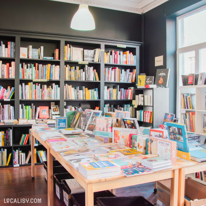 Coin lecture et culture dans la librairie, avec des étagères noires élégantes et des tables en bois disposant des ouvrages sur le cinéma, la musique et les grands penseurs. Une lampe suspendue éclaire l’espace de manière chaleureuse.